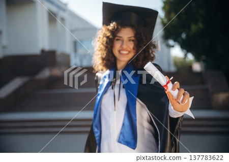 Finally finished, diploma in hand. Cheerful graduate student in a gown is standing outdoors 137783622