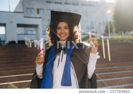 University building behind. Cheerful graduate student in a gown is standing outdoors 137783662