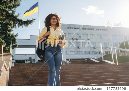 Ukrainian flag is behind. Beautiful woman student is near the university outdoors Ukrainian flag is behind. Beautiful woman student is near the university outdoors 137783696