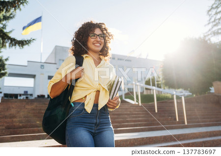 Ukrainian flag is behind. Beautiful woman student is near the university outdoors Ukrainian flag is behind. Beautiful woman student is near the university outdoors 137783697