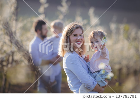 Spring portrait of parents with two small children on wlak in blooming orchard. 137783791