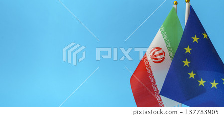 Flags of the European Union and Iran symbols isolated on an empty blue background. Conceptual photography showing international relations and foreign policy discussions between the EU and the Islamic 137783905