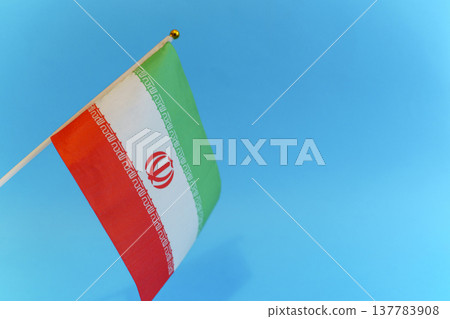 Iran flag against a blue sky background symbolizing political tension and crisis. Close-up view of the Iranian flag representing current geopolitical conflicts, social unrest, and international Iran flag against a blue sky background symbolizing political tension and crisis. Close-up view of the Iranian flag representing current geopolitical conflicts, social unrest, and international 137783908