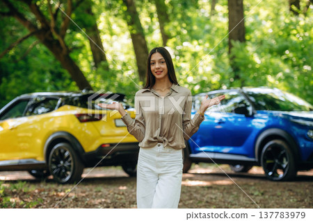 Choice between the blue or yellow ones. Young woman is in the forest with two cars Choice between the blue or yellow ones. Young woman is in the forest with two cars 137783979