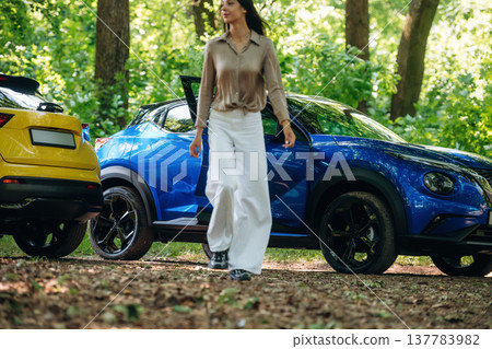 Posing for the camera. Young woman is in the forest with two cars 137783982