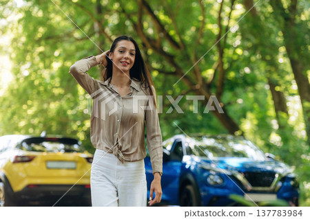 Posing for the camera. Young woman is in the forest with two cars 137783984