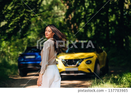 Posing for the camera. Young woman is in the forest with two cars Posing for the camera. Young woman is in the forest with two cars 137783985