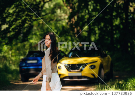 Posing for the camera. Young woman is in the forest with two cars Posing for the camera. Young woman is in the forest with two cars 137783986