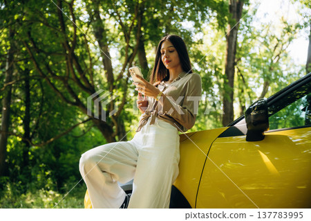 Smartphone is in hands. Woman is with her car in the forest Smartphone is in hands. Woman is with her car in the forest 137783995