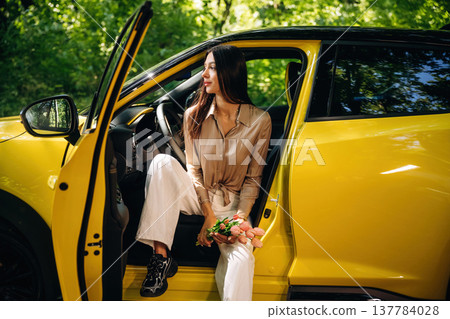Flowers are in hands. Woman is with her car in the forest 137784028