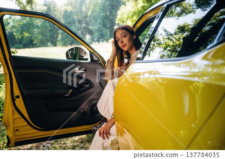 Looking at the camera, sitting with door opened. Woman is with her car in the forest 137784035