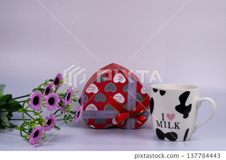 Red heart shaped gift box with ribbon, milk mug and purple flowers isolated on white background. Romantic celebration concept for Valentine, anniversary or special occasion. Red heart shaped gift box with ribbon, milk mug and purple flowers isolated on white background. Romantic celebration concept for Valentine, anniversary or special occasion. 137784443