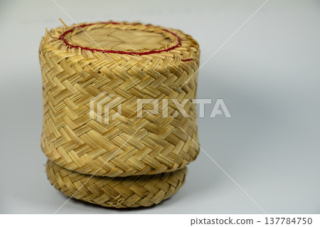 Traditional Thai woven bamboo container used to store cooked sticky rice. Handmade cylindrical basket with natural texture, isolated on white background. Traditional Thai woven bamboo container used to store cooked sticky rice. Handmade cylindrical basket with natural texture, isolated on white background. 137784750