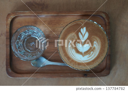 top view one coffee, water in clear glass and silver spoon on rectangular wooden tray on brown floor background, drink, cool, food, copy space top view one coffee, water in clear glass and silver spoon on rectangular wooden tray on brown floor background, drink, cool, food, copy space 137784782