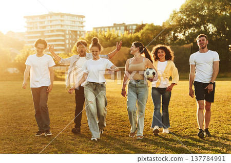 Walking forward. Young friends are having fun on the field with soccer ball 137784991