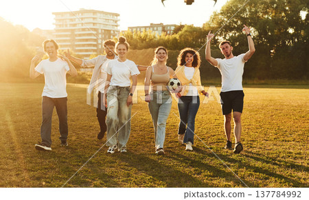 Walking forward. Young friends are having fun on the field with soccer ball 137784992