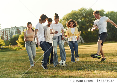 In the casual clothes. Group of friends are playing soccer on the field In the casual clothes. Group of friends are playing soccer on the field 137785032