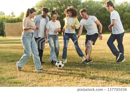 In the casual clothes. Group of friends are playing soccer on the field In the casual clothes. Group of friends are playing soccer on the field 137785036
