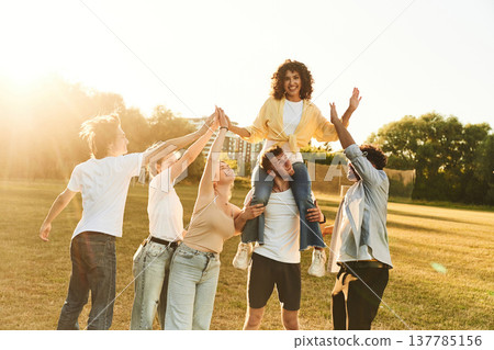 On the shoulders of the man, woman is sitting. Young friends are having fun on the field On the shoulders of the man, woman is sitting. Young friends are having fun on the field 137785156
