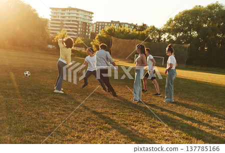 Under beautiful bright sunlight. Young friends are having fun on the field with soccer ball 137785166