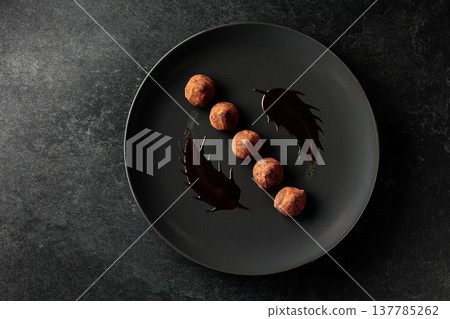 Chocolate truffles on a black plate. 137785262