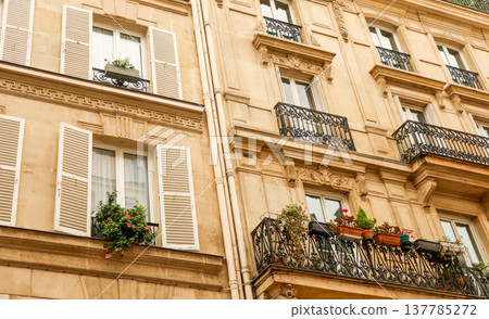 Parisian building facade showcasing Haussmann style architecture with decorative balconies, open window shutters, and flower boxes Parisian building facade showcasing Haussmann style architecture with decorative balconies, open window shutters, and flower boxes 137785272