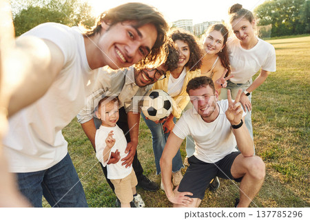 Handsome man is doing a selfie. Young friends are having fun on the field with soccer ball Handsome man is doing a selfie. Young friends are having fun on the field with soccer ball 137785296