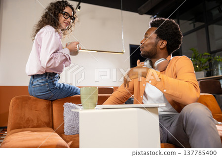Businesswoman holding coffee talking with man during work discussion 137785400