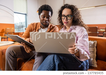 Wavy haired woman and man with laptop and tablet working together Wavy haired woman and man with laptop and tablet working together 137785435
