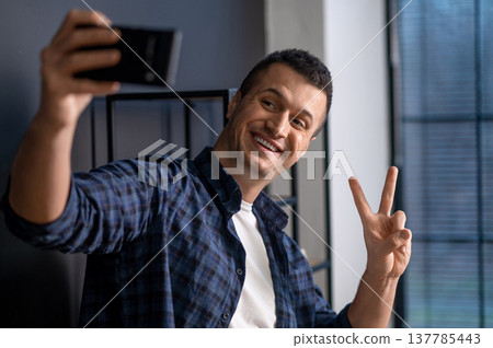 Playful man taking selfie with peace sign standing in office interior Playful man taking selfie with peace sign standing in office interior 137785443