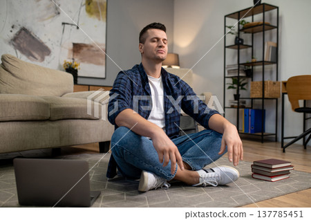 Peaceful man meditating with closed eyes on floor in modern living room Peaceful man meditating with closed eyes on floor in modern living room 137785451