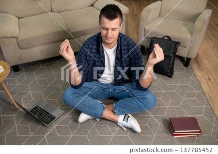 Relaxed man sitting in lotus position with eyes closed meditating on floor in living room Relaxed man sitting in lotus position with eyes closed meditating on floor in living room 137785452