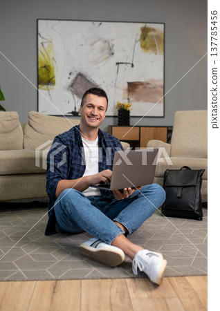 Man using laptop on floor in modern living room interior Man using laptop on floor in modern living room interior 137785456