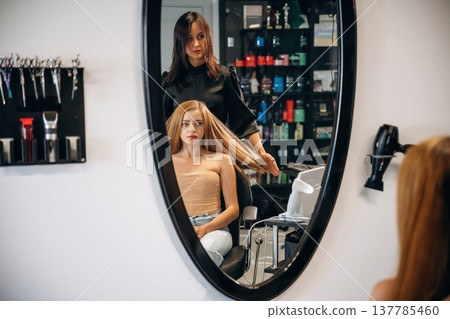 Customer is sitting on the chair. Woman is in a beauty salon with hair stylist 137785460