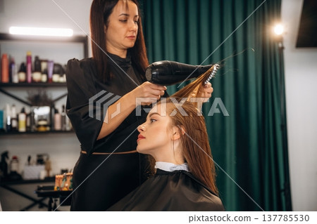 Drying the hair. Woman is in a beauty salon with hair stylist 137785530