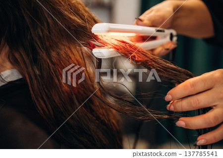 Straightening the hair. Woman is in a beauty salon with hair stylist Straightening the hair. Woman is in a beauty salon with hair stylist 137785541