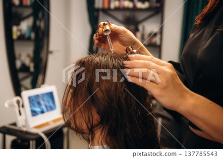 Drips serum onto head, hair roots. Woman is in a beauty salon with hair stylist Drips serum onto head, hair roots. Woman is in a beauty salon with hair stylist 137785543