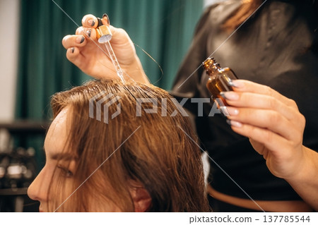 Drips serum onto head, hair roots. Woman is in a beauty salon with hair stylist Drips serum onto head, hair roots. Woman is in a beauty salon with hair stylist 137785544