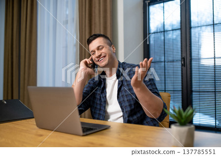Cheerful man multitasking on phone and laptop in office interior 137785551