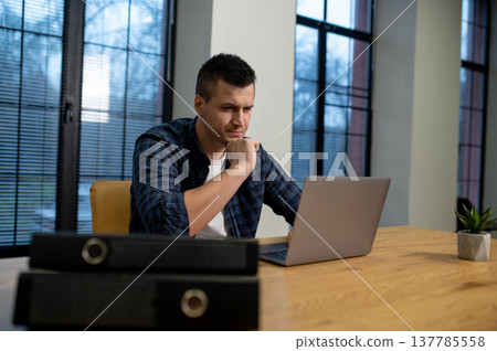 Pensive man working on laptop and touching forehead at wooden table in office Pensive man working on laptop and touching forehead at wooden table in office 137785558