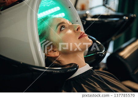Green color. Woman is in a beauty salon with LED hair growth helmet 137785570