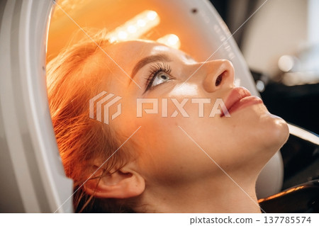 Yellow color. Woman is in a beauty salon with LED hair growth helmet Yellow color. Woman is in a beauty salon with LED hair growth helmet 137785574