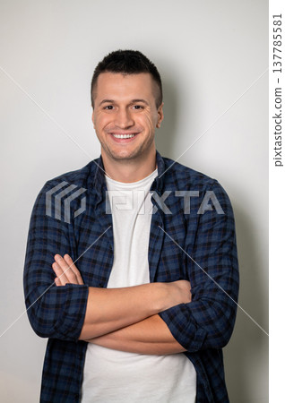 Self-assured man posing with crossed arms against white wall 137785581