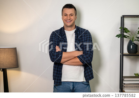 Confident man standing with crossed arms posing in modern home interior Confident man standing with crossed arms posing in modern home interior 137785582