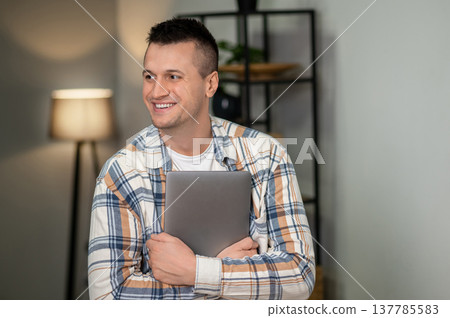 Confident male holding laptop in home workspace Confident male holding laptop in home workspace 137785583