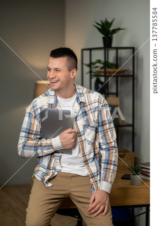 Man standing with laptop in contemporary home office interior Man standing with laptop in contemporary home office interior 137785584