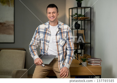 Confident man holding laptop standing in home office interior Confident man holding laptop standing in home office interior 137785585
