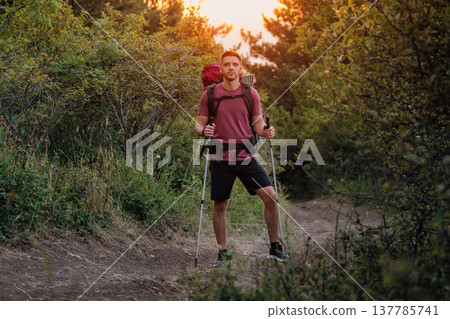 Handsome hiker trekking through forest path with backpack and poles at sunset. Active adventure hiking Handsome hiker trekking through forest path with backpack and poles at sunset. Active adventure hiking 137785741