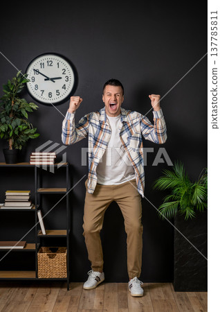 Overjoyed man celebrating victory with raised fists standing in modern interior Overjoyed man celebrating victory with raised fists standing in modern interior 137785811
