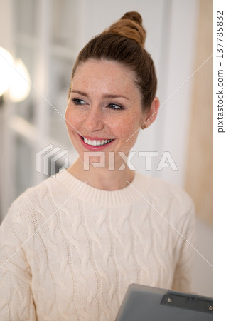 Waist up of smiling woman with hair bun in white sweater 137785832